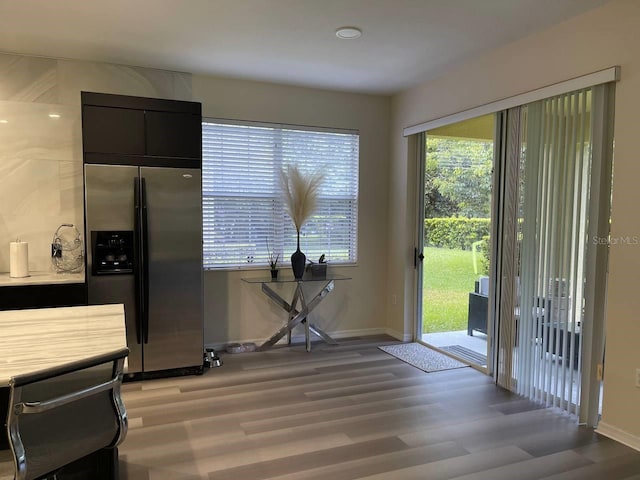 interior space featuring light wood-type flooring, stainless steel refrigerator with ice dispenser, dark cabinetry, light countertops, and baseboards