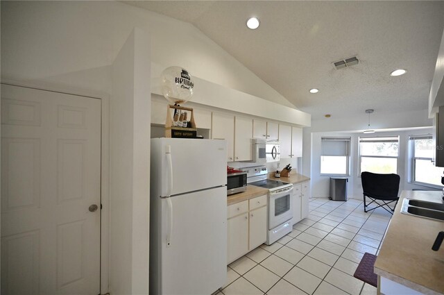 kitchen with a textured ceiling, white appliances, light tile patterned floors, lofted ceiling, and white cabinets