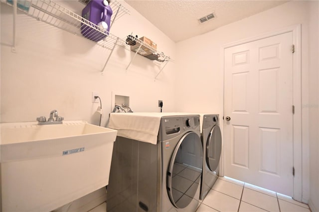 washroom featuring light tile patterned floors, a textured ceiling, independent washer and dryer, and sink