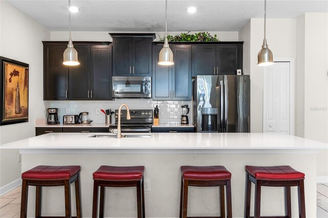 1224 Challenge Dr, Davenport, FL 33896 - kitchen featuring appliances with stainless steel finishes, a breakfast bar, light countertops, a kitchen island with sink, and decorative backsplash