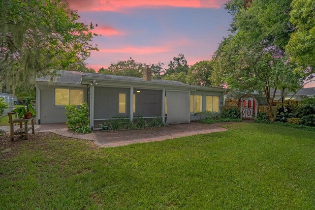 back house at dusk with a lawn and a patio area