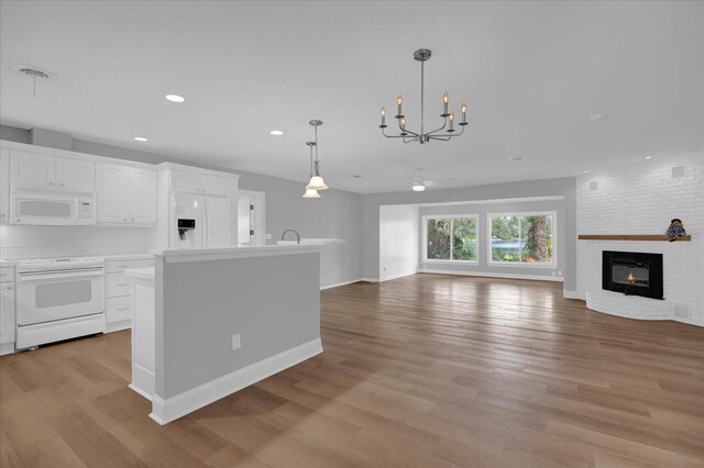 kitchen with a brick fireplace, white appliances, decorative light fixtures, a center island, and white cabinetry