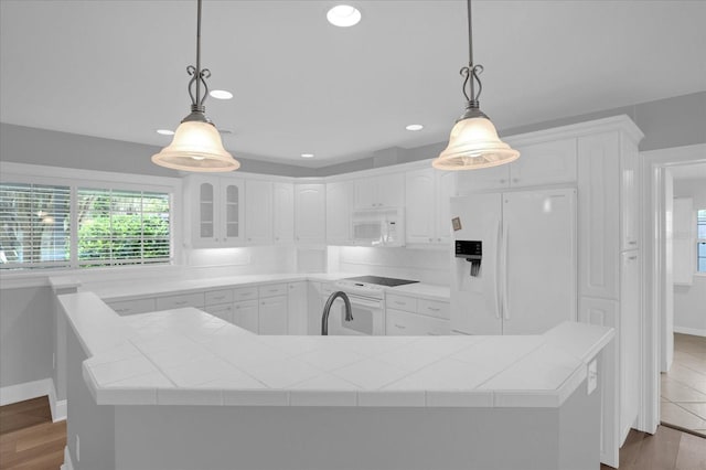 kitchen featuring white appliances, a center island with sink, white cabinets, tile countertops, and wood finished floors