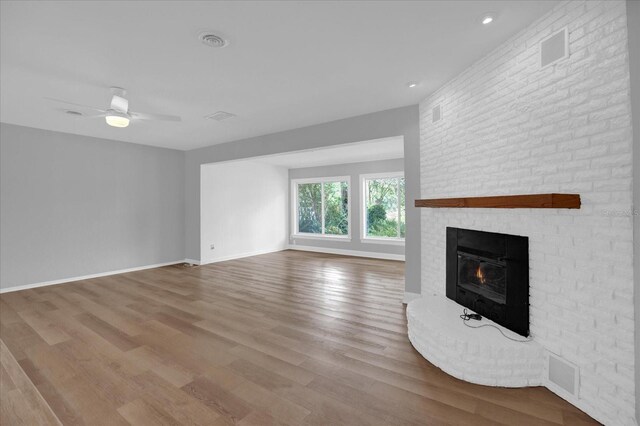 unfurnished living room with light hardwood / wood-style flooring, a brick fireplace, ceiling fan, and brick wall