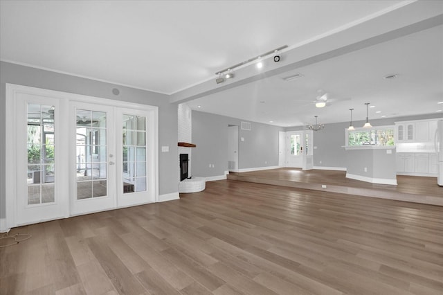 unfurnished living room with light wood-style flooring, a fireplace, baseboards, french doors, and rail lighting