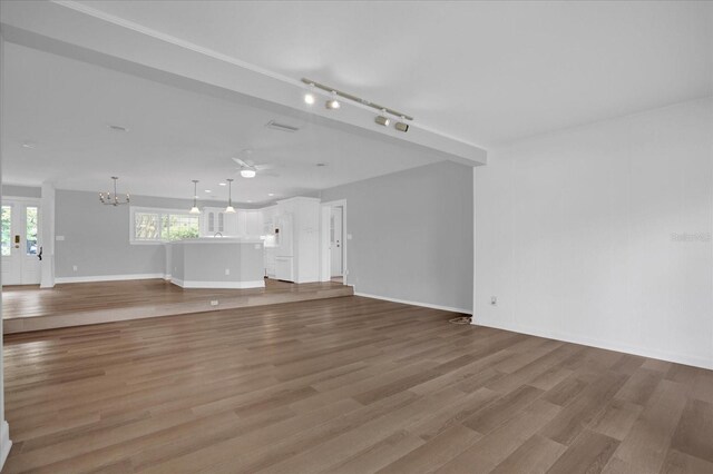 unfurnished living room featuring ceiling fan with notable chandelier, rail lighting, and light hardwood / wood-style flooring