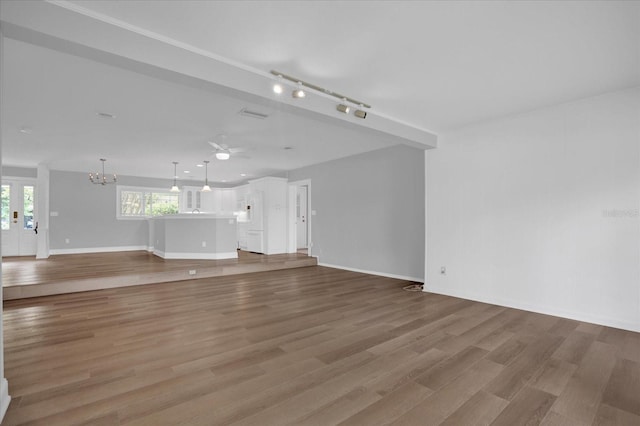 unfurnished living room featuring light wood-style floors, track lighting, baseboards, and ceiling fan with notable chandelier