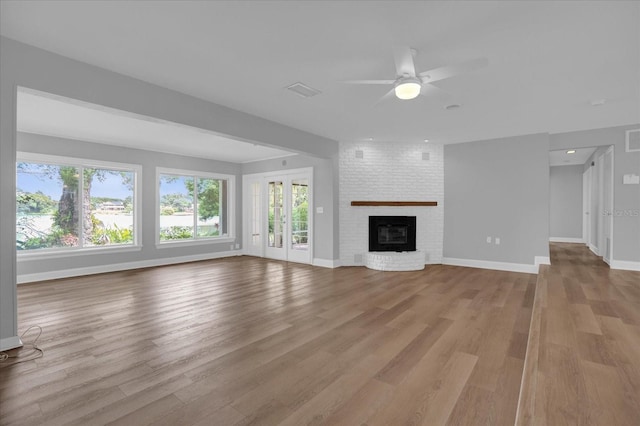 unfurnished living room featuring ceiling fan, a fireplace, visible vents, baseboards, and light wood finished floors