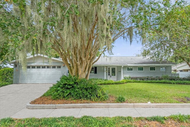 single story home with a front yard, concrete driveway, brick siding, and an attached garage