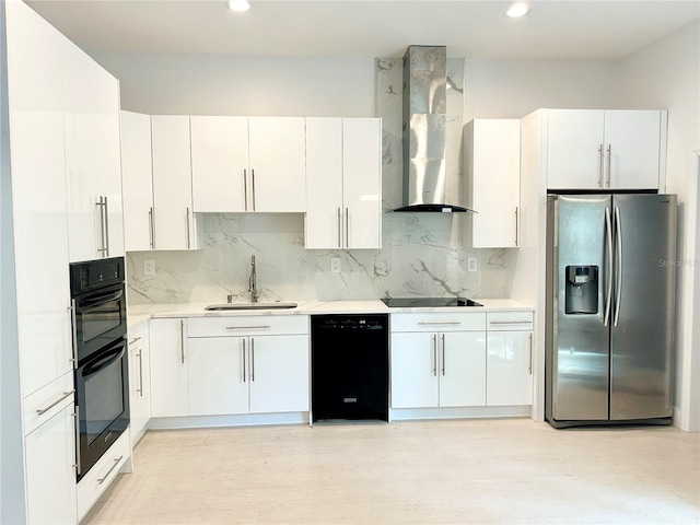 kitchen with wall chimney exhaust hood, black appliances, backsplash, sink, and white cabinets