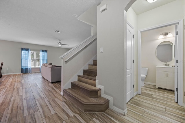 staircase featuring a textured ceiling, wood-type flooring, and ceiling fan