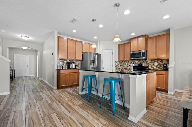 kitchen with hanging light fixtures, light hardwood / wood-style floors, stainless steel appliances, a textured ceiling, and a center island with sink