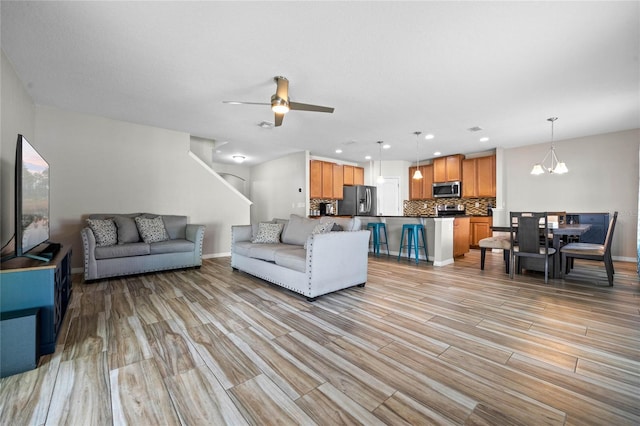 living room featuring ceiling fan with notable chandelier and light wood-type flooring