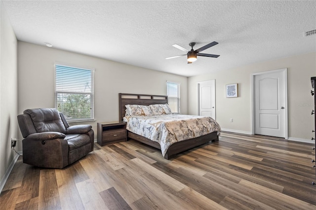 bedroom with ceiling fan, a textured ceiling, dark wood-type flooring, and multiple windows