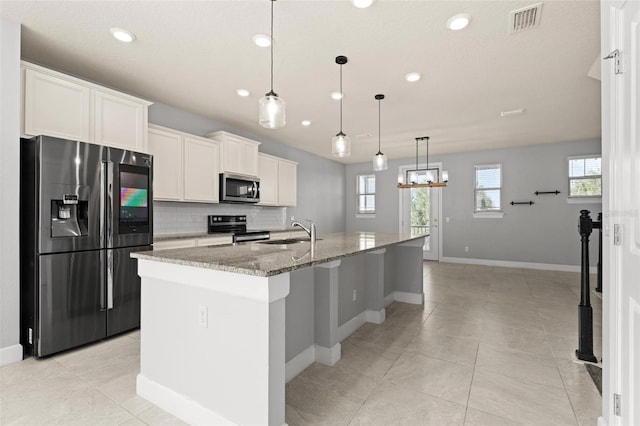 kitchen with stainless steel appliances, stone countertops, white cabinetry, sink, and a kitchen island with sink