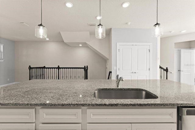 kitchen with decorative light fixtures, stainless steel dishwasher, stone counters, and sink