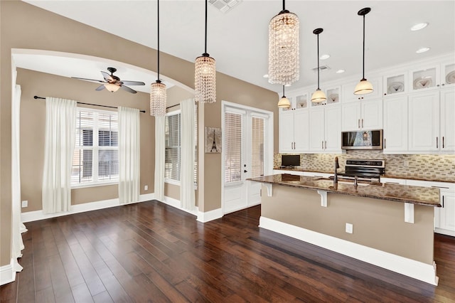 kitchen with a center island with sink, pendant lighting, dark stone countertops, and white cabinets