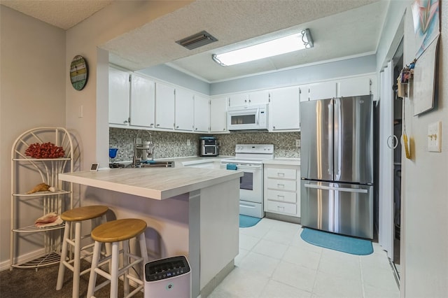 kitchen with white cabinetry, white appliances, kitchen peninsula, sink, and a breakfast bar