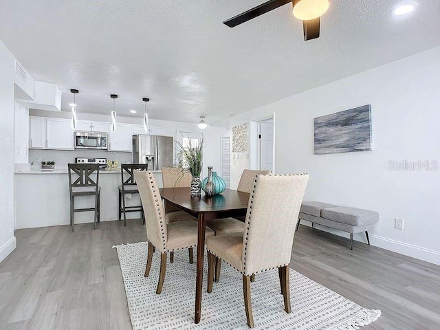 dining space with a textured ceiling, ceiling fan, and light hardwood / wood-style floors