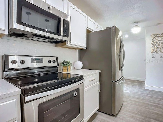 kitchen with appliances with stainless steel finishes, a textured ceiling, white cabinetry, and light hardwood / wood-style flooring