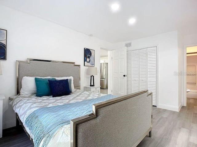 bedroom featuring a closet, connected bathroom, stainless steel refrigerator, and light hardwood / wood-style floors