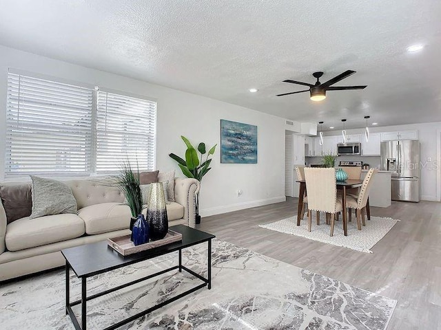 living room featuring light wood-type flooring, a textured ceiling, and ceiling fan