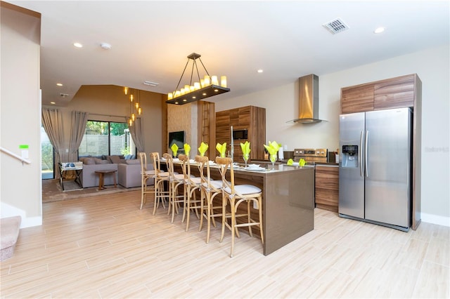 kitchen with stainless steel appliances, a kitchen breakfast bar, decorative light fixtures, a kitchen island, and wall chimney exhaust hood