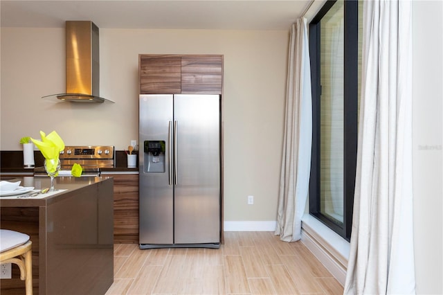 kitchen with light wood-type flooring, stainless steel appliances, and wall chimney exhaust hood