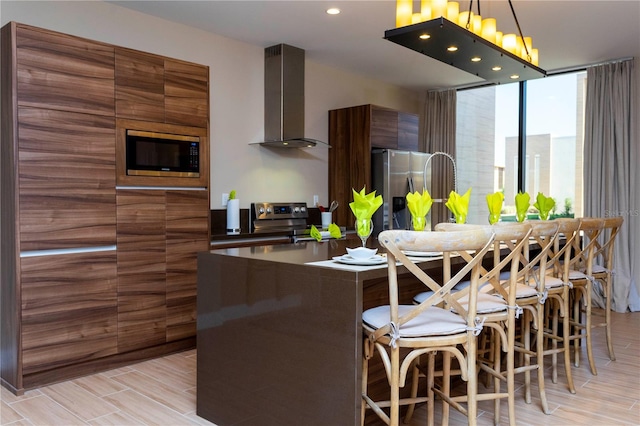 kitchen with wall chimney range hood, a kitchen bar, stainless steel appliances, and light hardwood / wood-style flooring