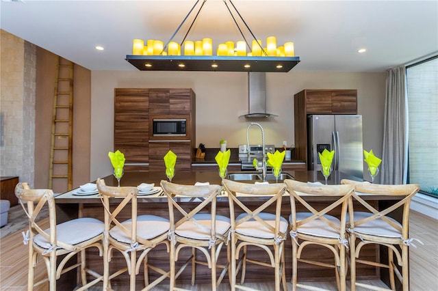 kitchen with light hardwood / wood-style flooring, stainless steel appliances, an inviting chandelier, sink, and wall chimney range hood