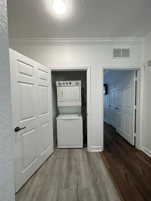 clothes washing area with hardwood / wood-style floors, stacked washing maching and dryer, a textured ceiling, and ornamental molding