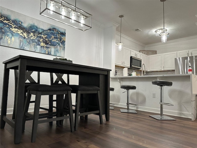 interior space with dark hardwood / wood-style floors, a kitchen bar, kitchen peninsula, stainless steel appliances, and white cabinetry