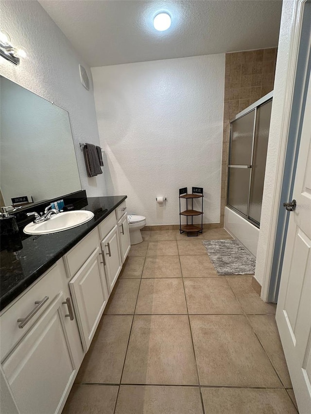 full bathroom featuring tile patterned flooring, toilet, shower / bath combination with glass door, vanity, and a textured ceiling