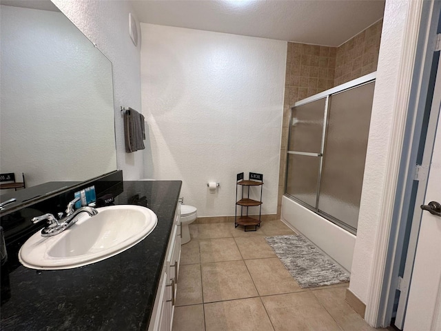 full bathroom with a textured ceiling, vanity, bath / shower combo with glass door, tile patterned flooring, and toilet