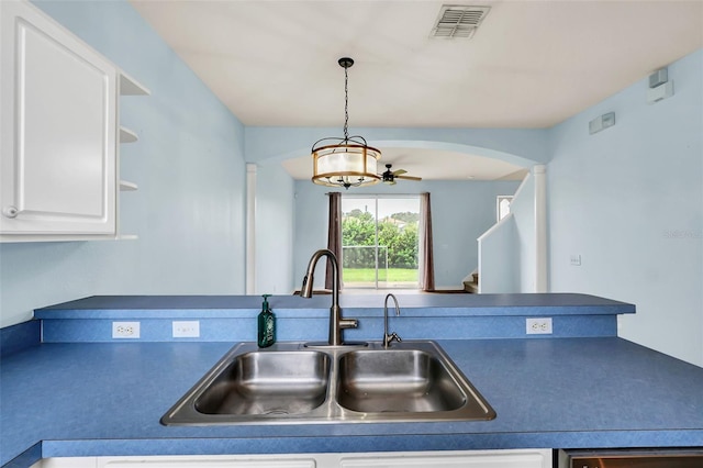 kitchen with arched walkways, dark countertops, visible vents, white cabinets, and a sink