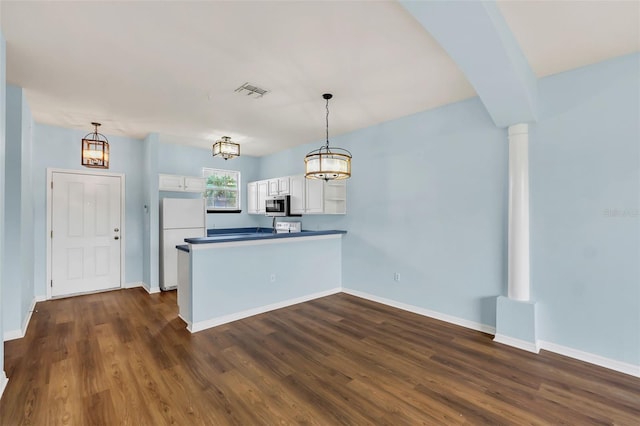 kitchen with dark wood-style floors, stainless steel microwave, freestanding refrigerator, white cabinets, and a peninsula