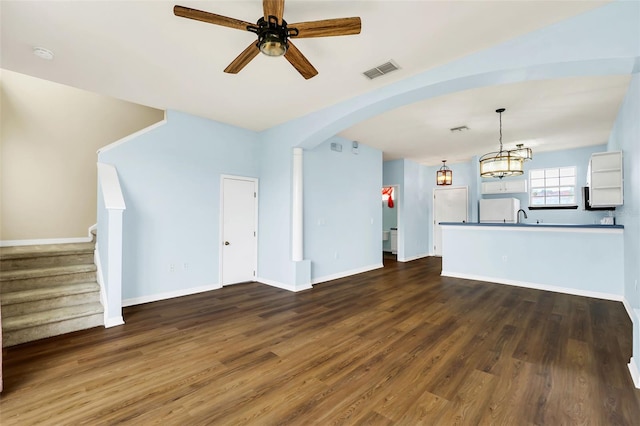 unfurnished living room featuring dark wood-style floors, arched walkways, visible vents, stairway, and a ceiling fan