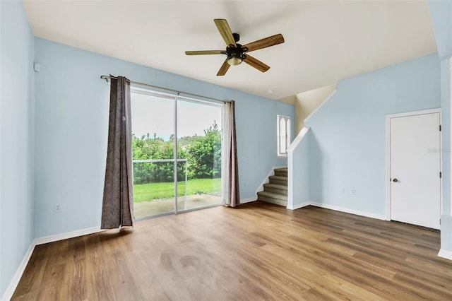 unfurnished living room with ceiling fan, stairway, baseboards, and wood finished floors