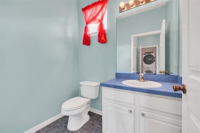 bathroom with stacked washer and clothes dryer, toilet, vanity, baseboards, and tile patterned floors