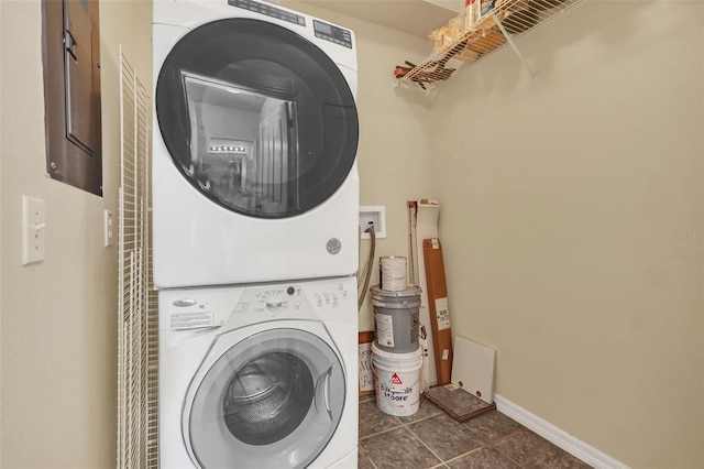 laundry room with laundry area, dark tile patterned flooring, stacked washer and clothes dryer, and baseboards