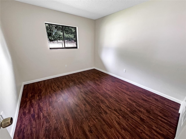 empty room featuring dark wood finished floors, a textured ceiling, and baseboards