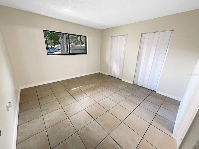 unfurnished bedroom with baseboards, a textured ceiling, and multiple closets