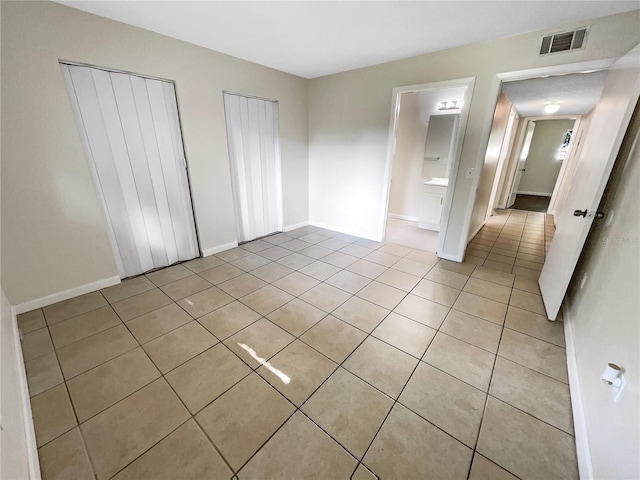 unfurnished bedroom with light tile patterned flooring, two closets, visible vents, and baseboards