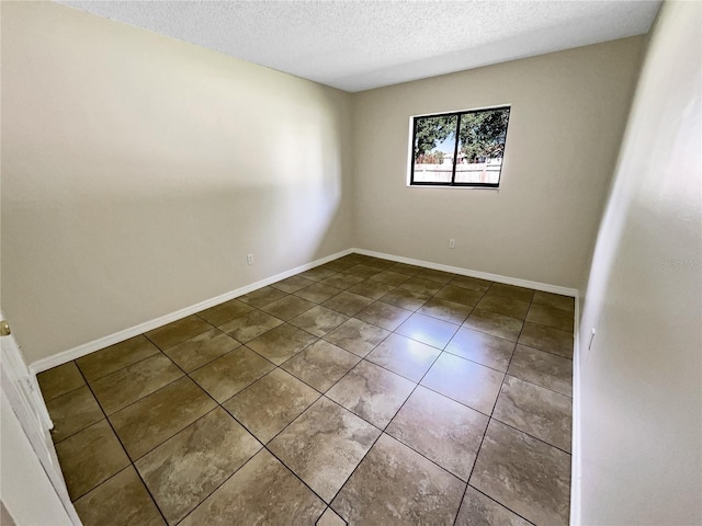 tiled spare room featuring a textured ceiling and baseboards