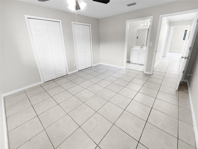 unfurnished bedroom featuring light tile patterned floors, ceiling fan, ensuite bath, and two closets