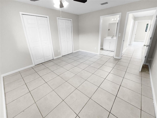 unfurnished bedroom with light tile patterned floors, a ceiling fan, baseboards, visible vents, and multiple closets