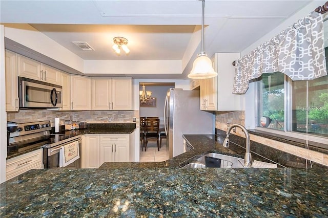 kitchen featuring dark stone counters, a chandelier, stainless steel appliances, and sink