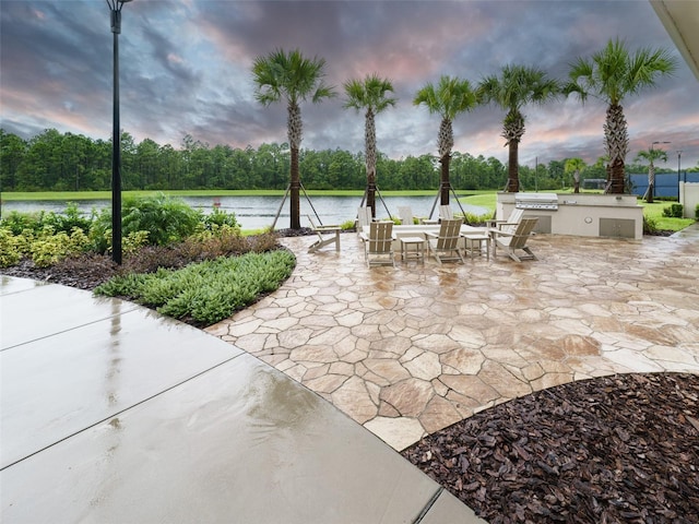 patio terrace at dusk with exterior kitchen, a water view, and area for grilling