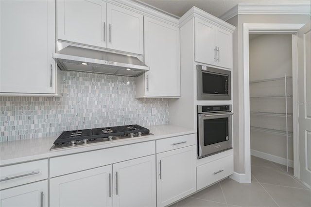 kitchen featuring ornamental molding, white cabinetry, light tile patterned floors, range hood, and appliances with stainless steel finishes