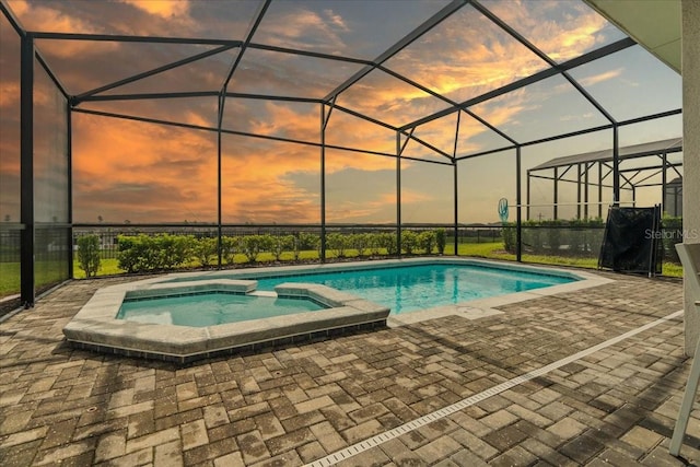 pool at dusk with a patio, glass enclosure, and an in ground hot tub